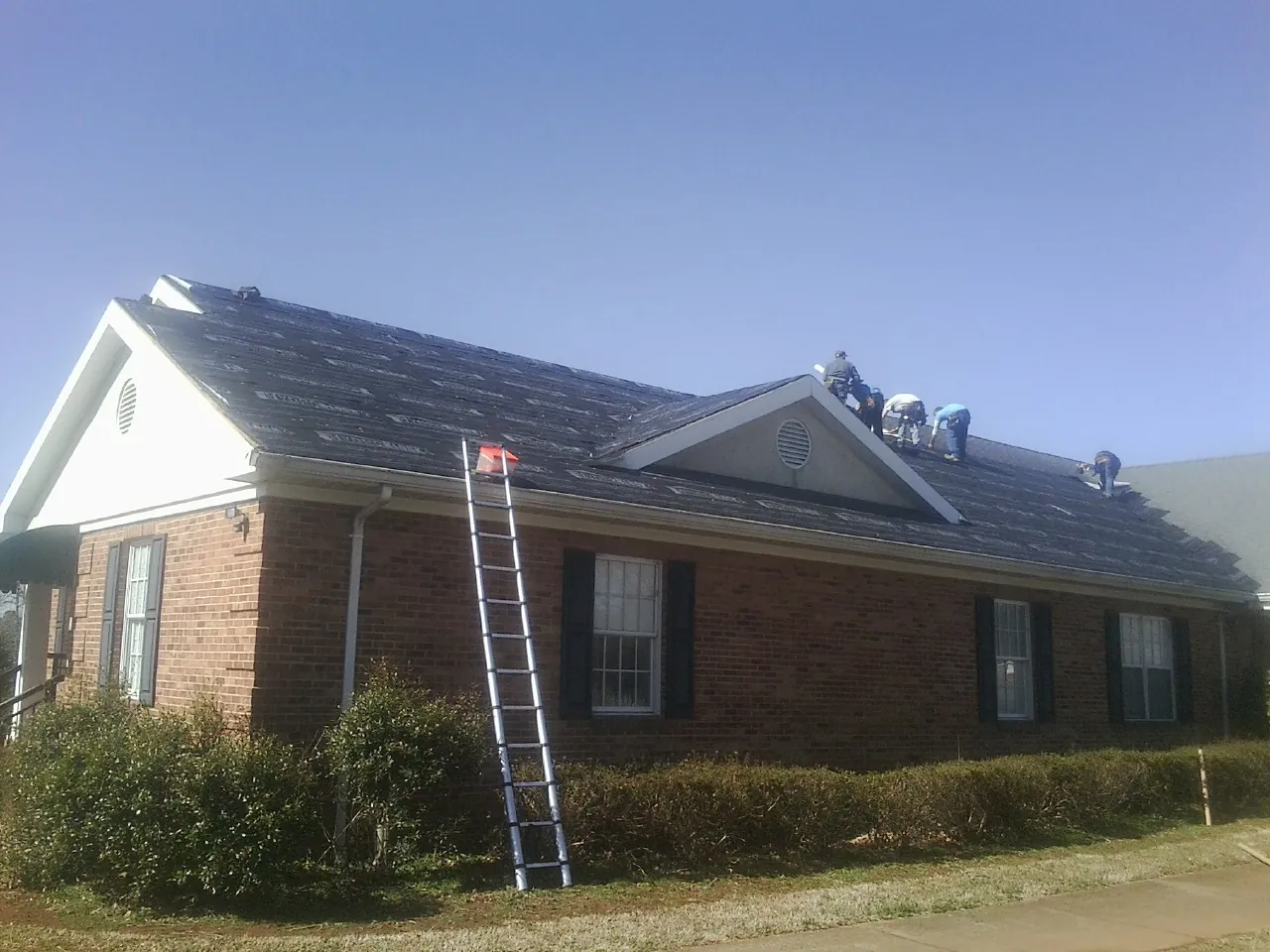 Crew tearing shingles off a brick ranch roof with a ladder set — Metal Roof Repair work by our crew in Dawson Springs
