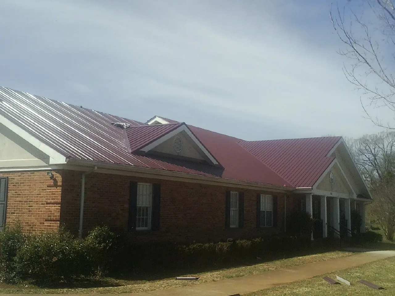 Red metal roof with gabled entries on a long brick building, from a Hail Damage Roof Repair job in Dawson Springs