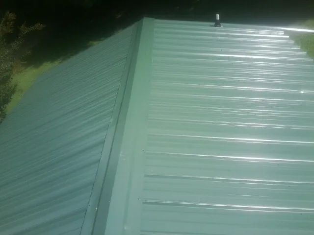 New green metal panels meeting at the ridge of a roof — Flat Roof Repair work by our crew in Dawson Springs