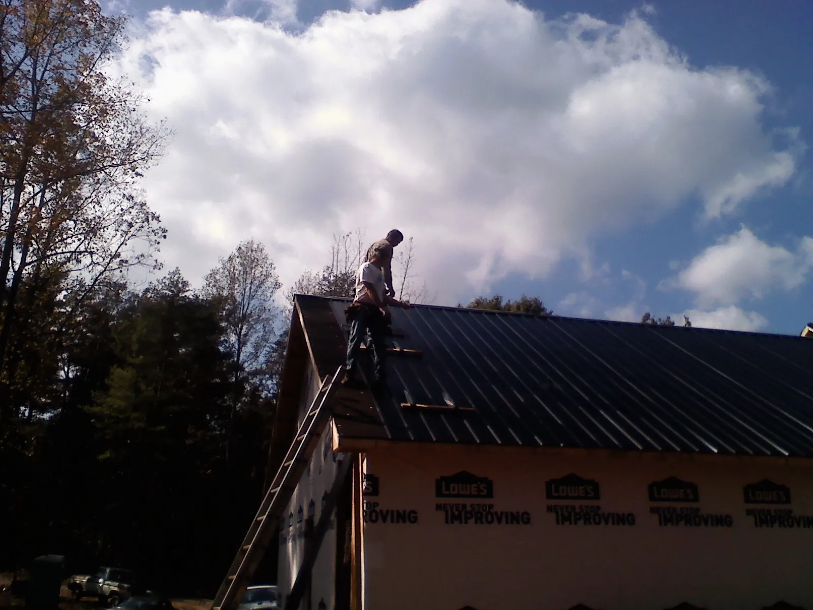 Roofer fastening dark metal panels high against a cloudy sky, from a Roof Inspection job in Dawson Springs
