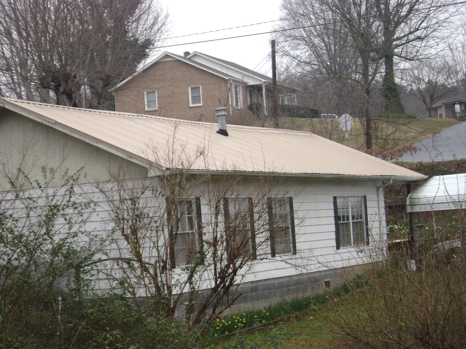 Tan metal roof on a white sided house set into a hillside — Commercial Roofing by Roofing Brothers in Dawson Springs